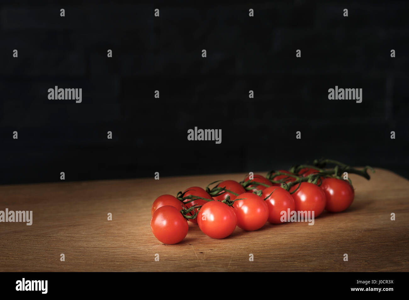 Zweig Cherrytomaten auf einem Holztisch vor einem dunklen Hintergrund, gesunde Ernährung Konzept liegen. Stockfoto