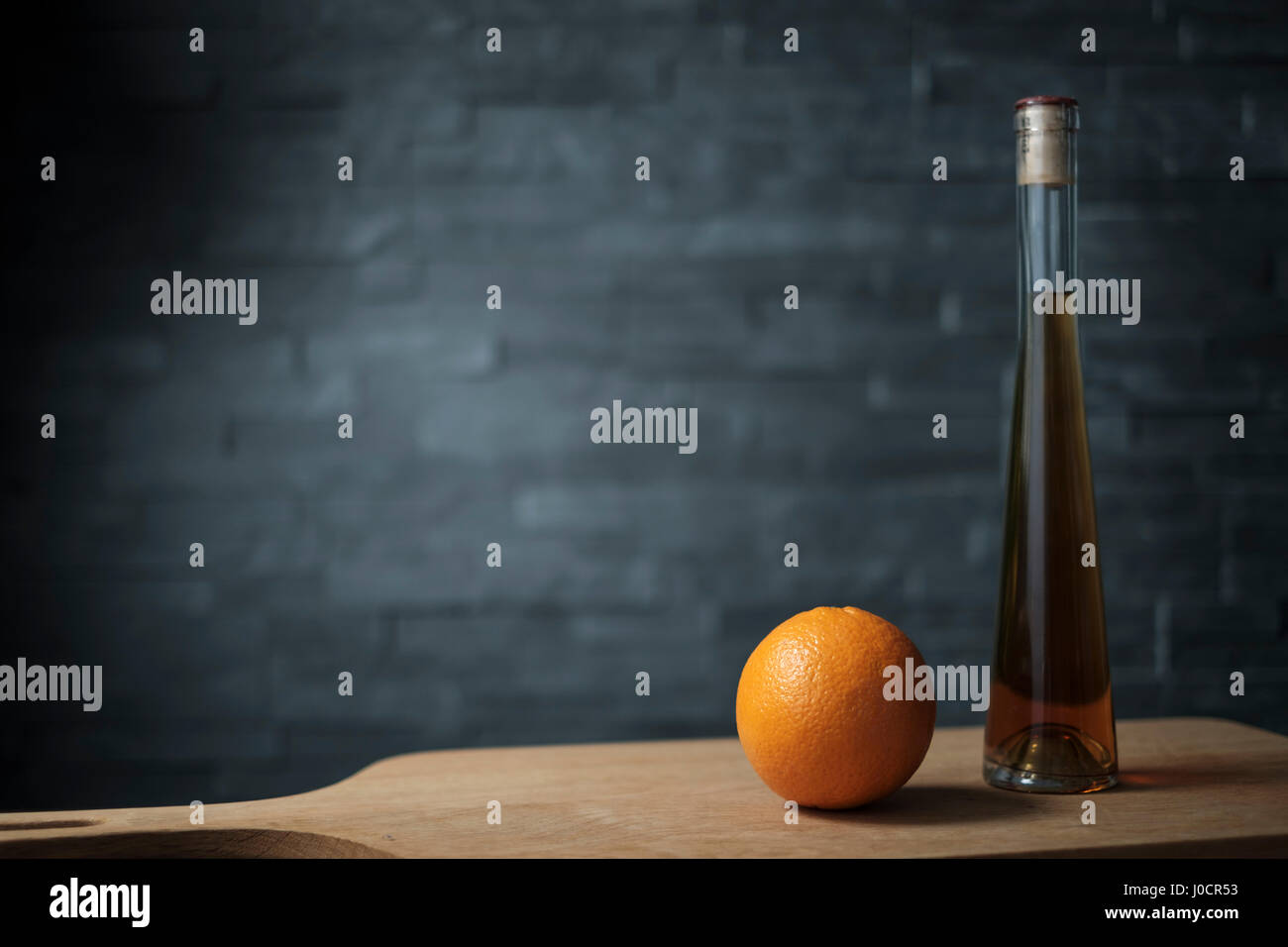 Orange mit einer Flasche Schnaps auf einem Holzbrett vor einem dunklen Hintergrund Stockfoto