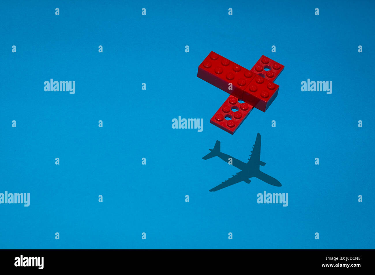 Flugzeug in Lego rote Backstein auf eine blaue Schrift mit dem Schatten eines realen Flugzeugs gebaut. Stockfoto