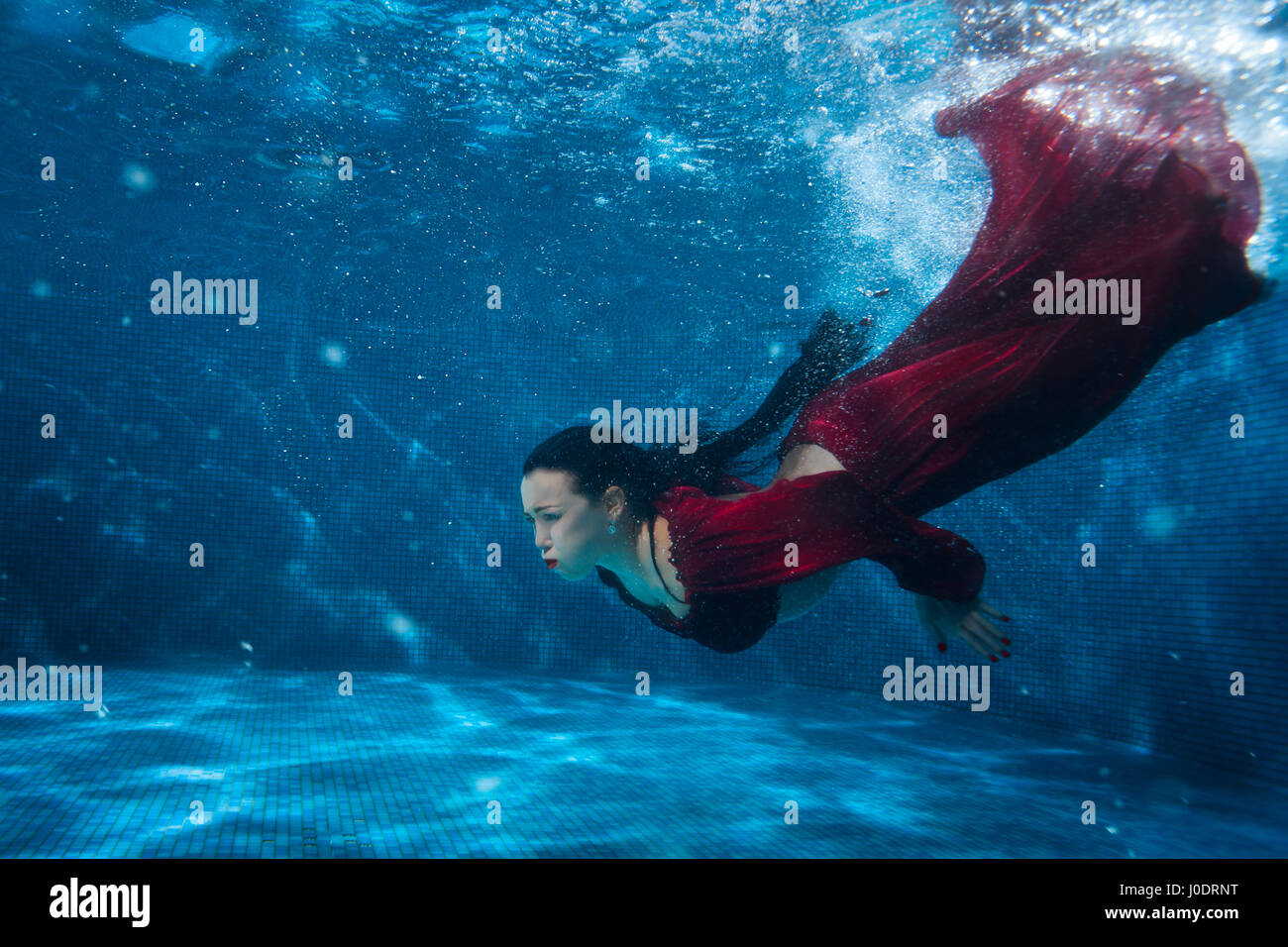 Frau im roten Kleid taucht unter Wasser im Pool. Stockfoto