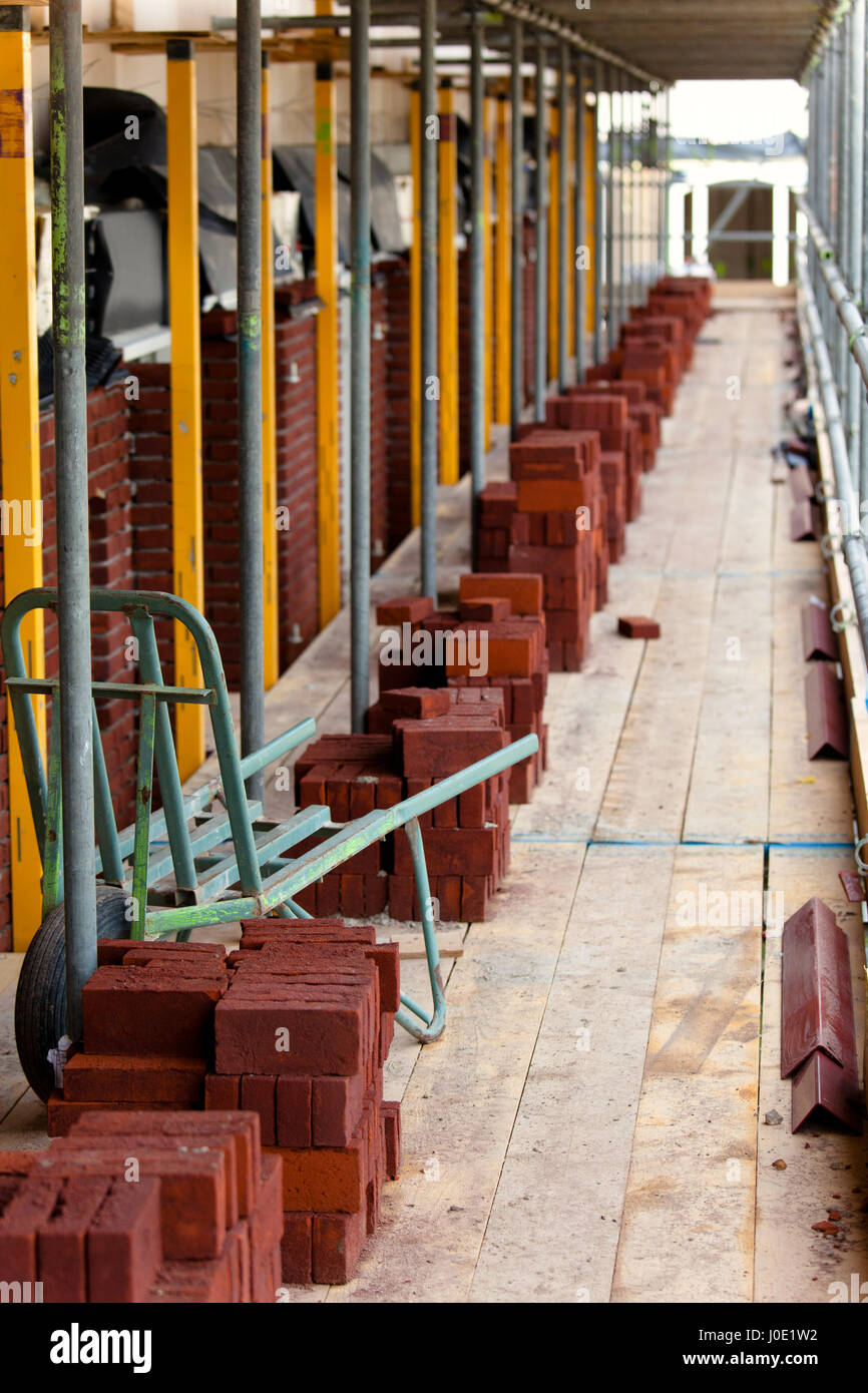 rote Ziegel und Schubkarre auf Gerüsten Stockfoto