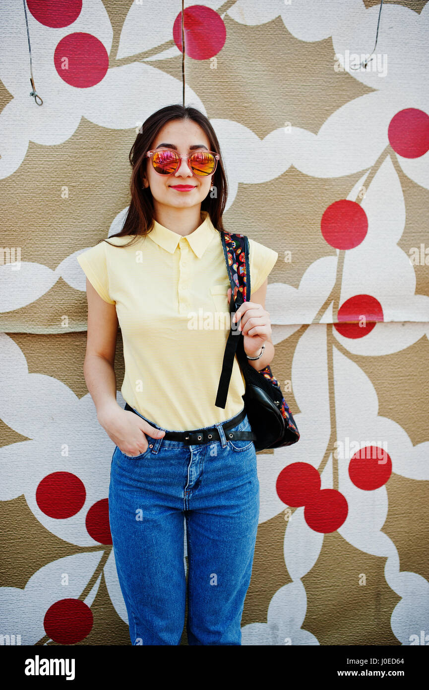 Junge Teenager-Mädchen gegen gedruckte Wand auf gelben T-shirt, Jeans und eine Sonnenbrille tragen. Stockfoto