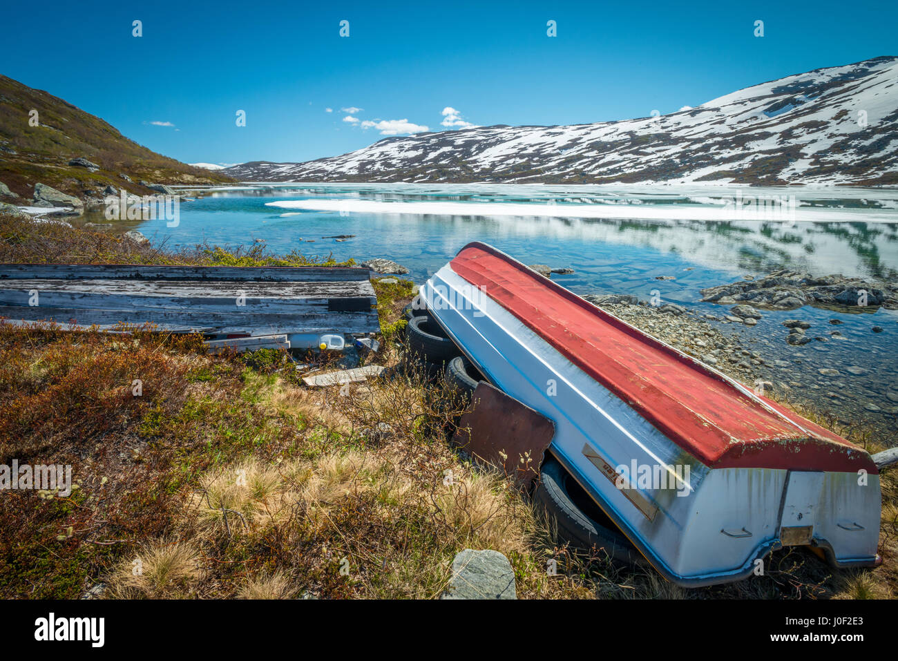 Alte Boote liegen verlassene am Rande ein Bergsee bis in den verschneiten Bergen Stockfoto