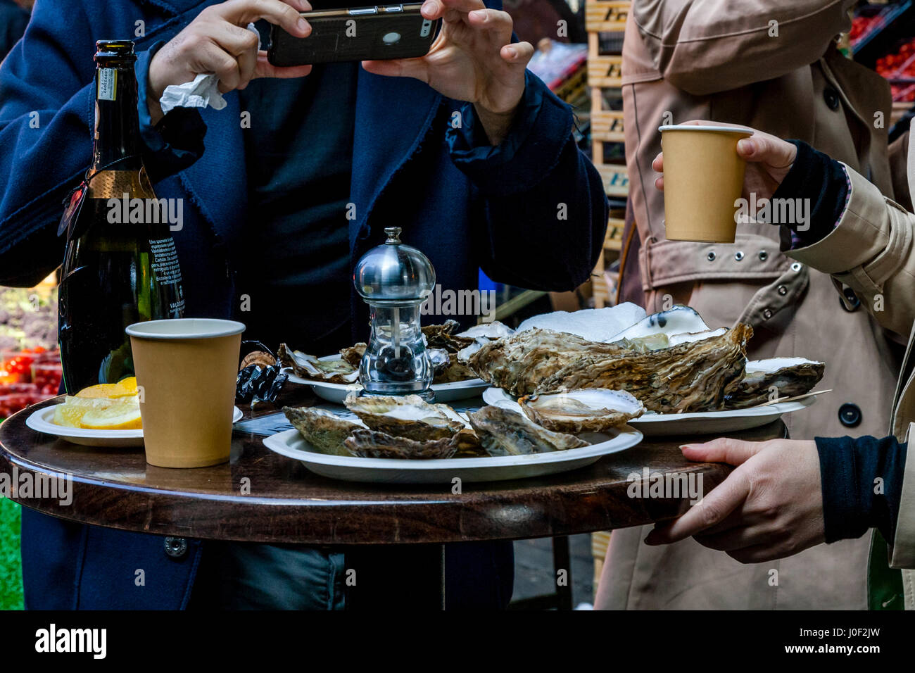 Ein junger Mann fotografiert sein Mittagessen Prosecco und Austern im Borough Market, London, England Stockfoto