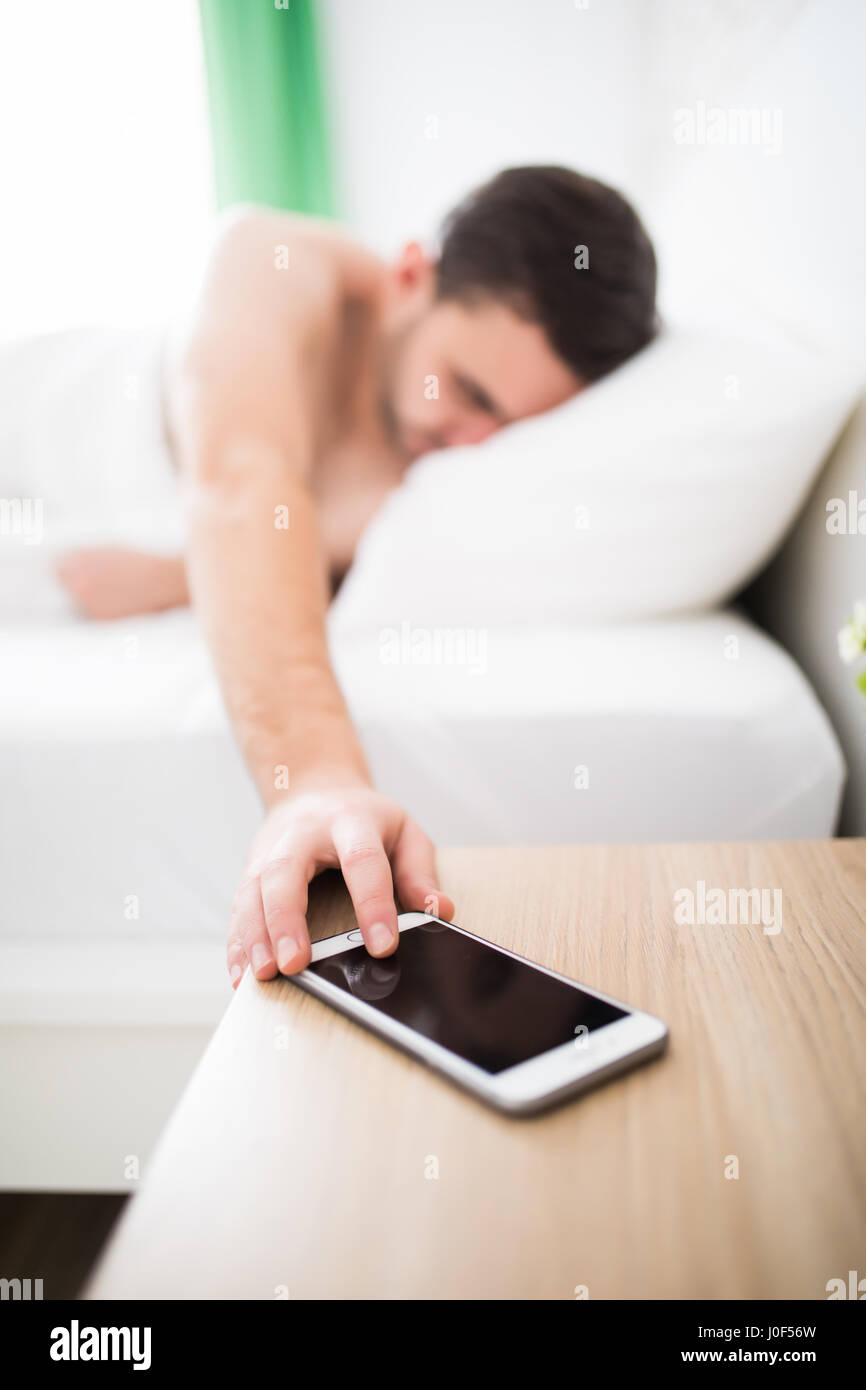 Schöner junger Mann mit Handy Wecker aufwachen Stockfotografie - Alamy