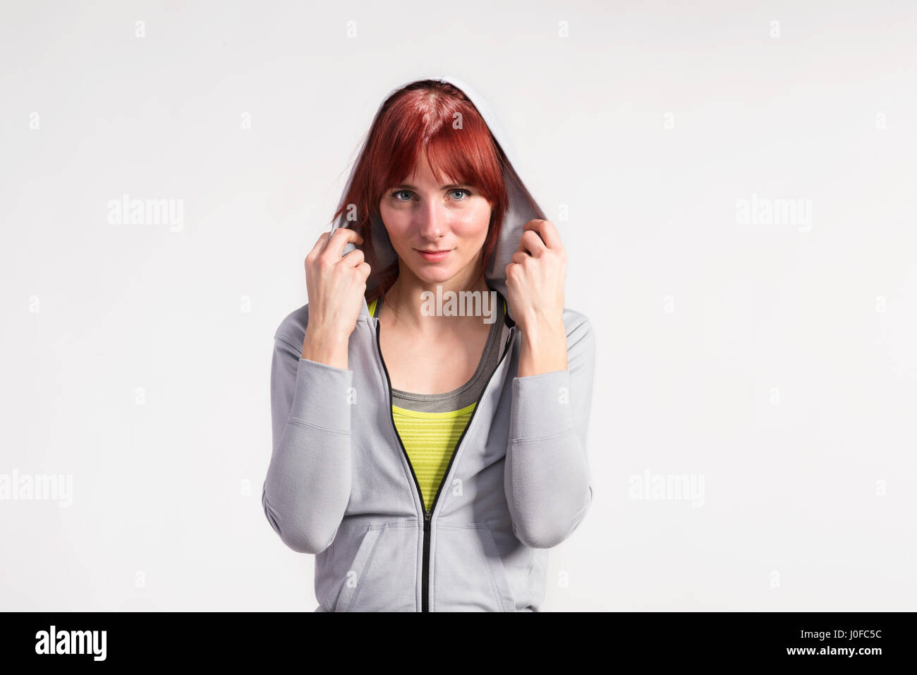 Attraktive junge Fitness-Frau in grauen Sweatshirt mit Kapuze. Studio auf grauem Hintergrund gedreht. Stockfoto
