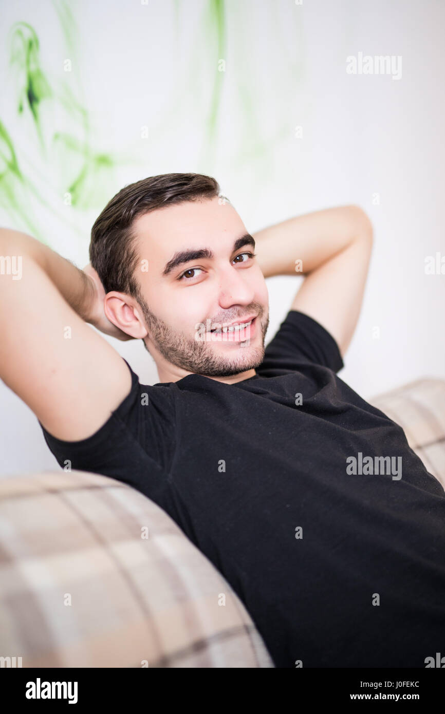 Gut aussehender Mann mit Händen hinter dem Kopf auf Sofa zu Hause Stockfoto