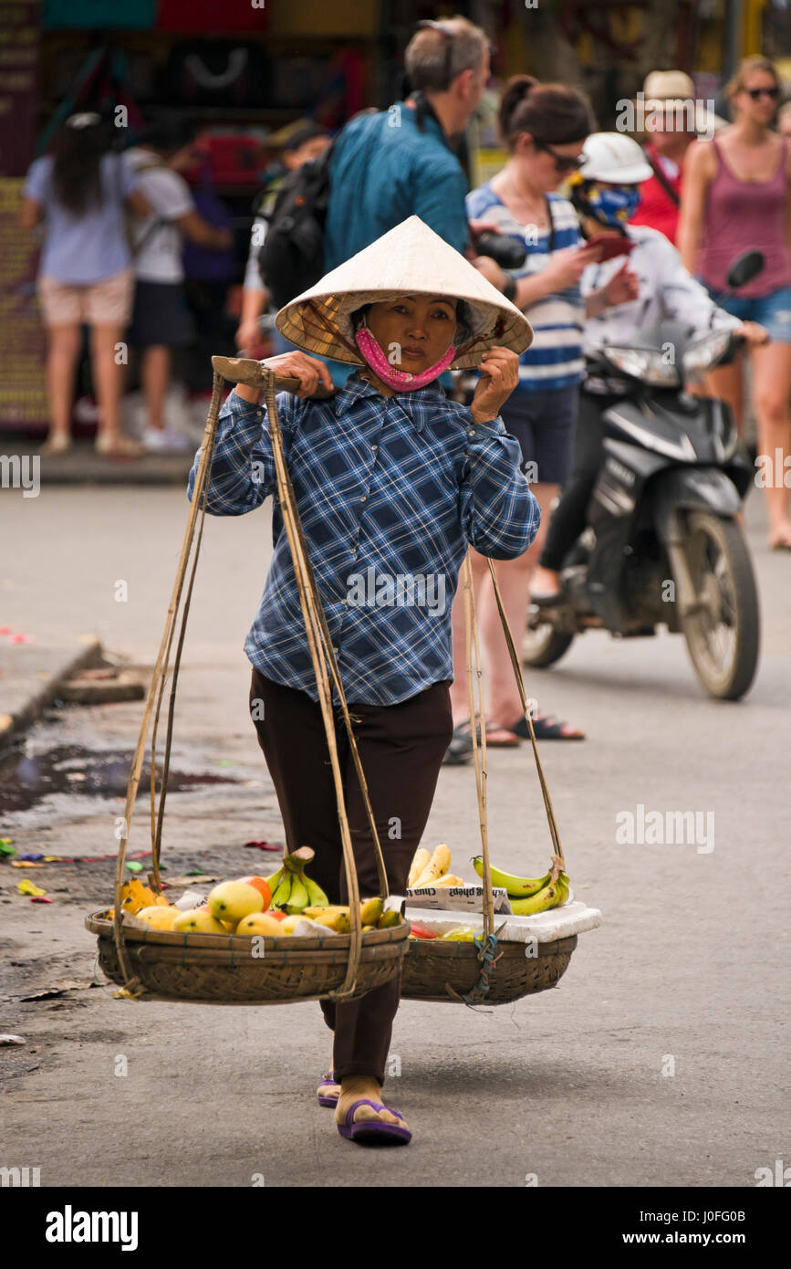 Vertikale Porträt einer vietnamesischen Frau trägt ein traditionelles Bambus Joch in Hoi an, Vietnam. Stockfoto