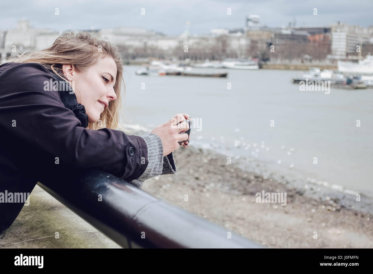 Technologie: Eine junge attraktive Frau mit dem Fotografieren mit ihrem Handy von der Themse, London South Bank. Stockfoto