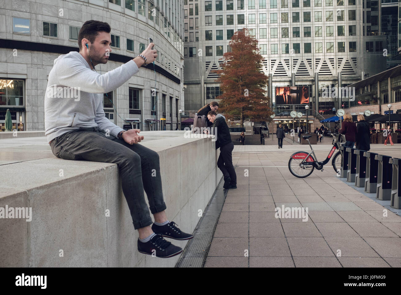 Technologie: Ein hübsches junge kaukasisches Männchen dauert eine Selfie saßen draußen Canary Wharf, London. Stockfoto