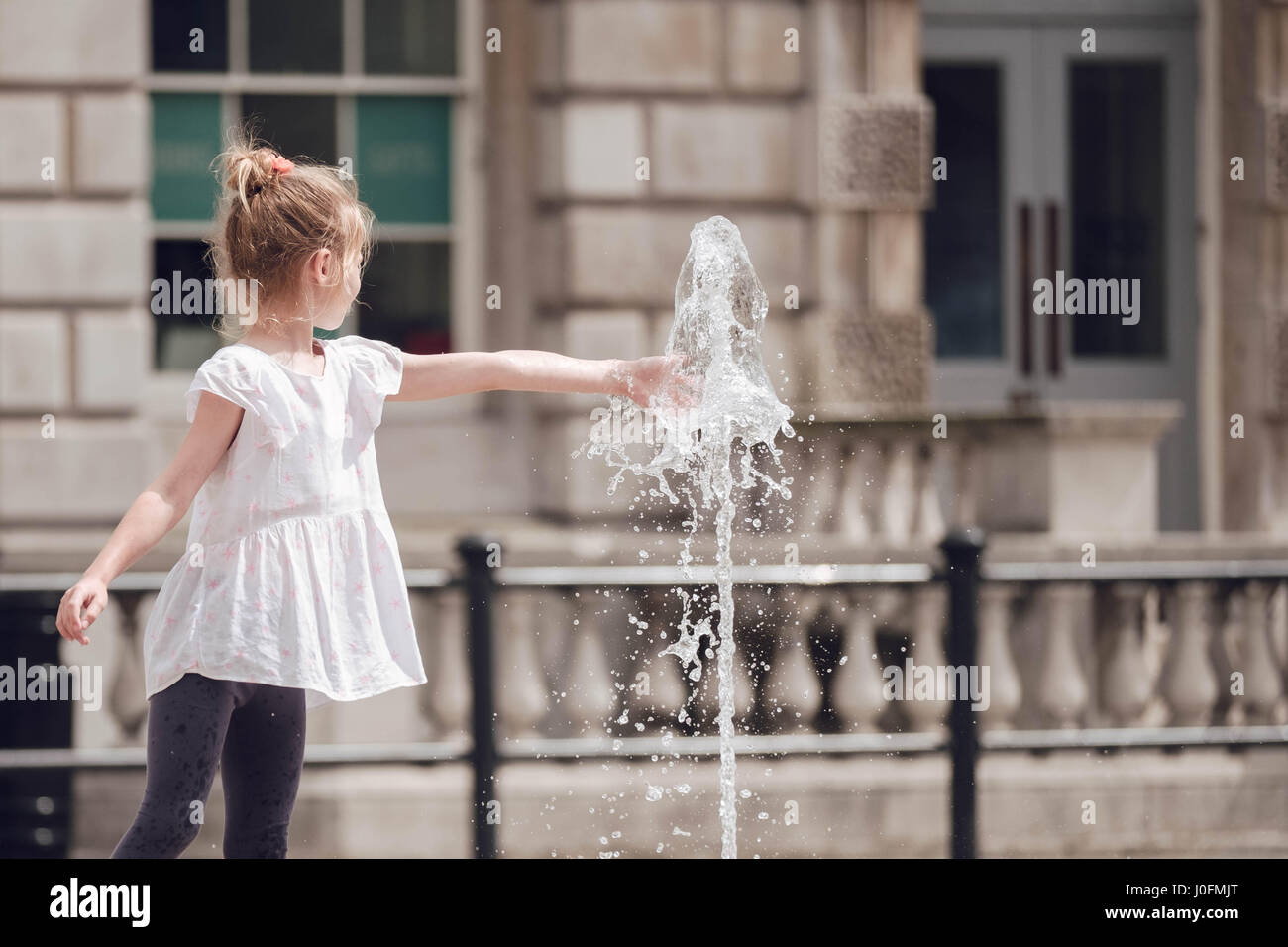 Ein junges Mädchen streckt und legt ihre Hand auf dem Wasserbrunnen am Somerset House, The Strand in London an einem heißen Sommertag im Jahr 2016. Stockfoto