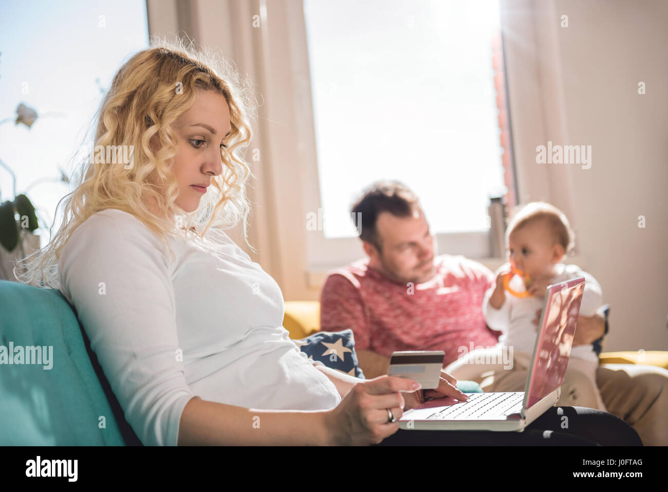 Frau online-shopping mit Kreditkarte mit ihrem Mann und Kind im Hintergrund Stockfoto