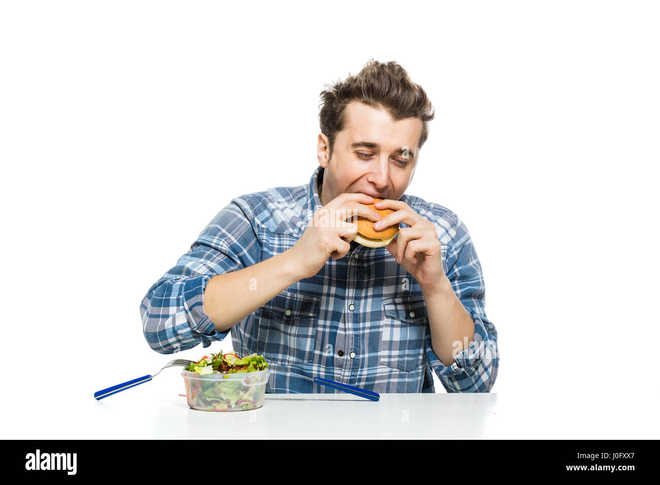 Fastfood im Vergleich zu gesunden Lebensmitteln Konzept mit jungen Mann einen Hamburger Essen und Salat auseinander zu verlassen Stockfoto