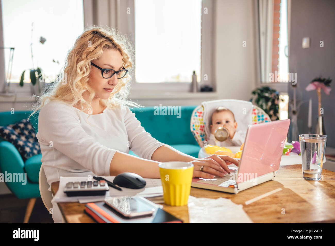 Mutter trägt Brille Büro am Laptop zu Hause arbeiten und kümmert sich um ihr baby Stockfoto