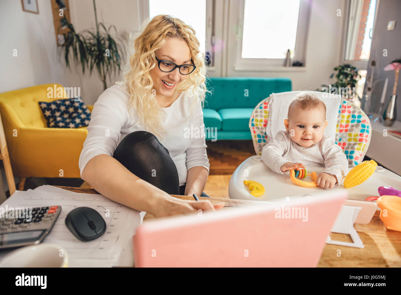 Mutter trägt Brille Büro am Laptop zu Hause arbeiten und kümmert sich um ihr baby Stockfoto