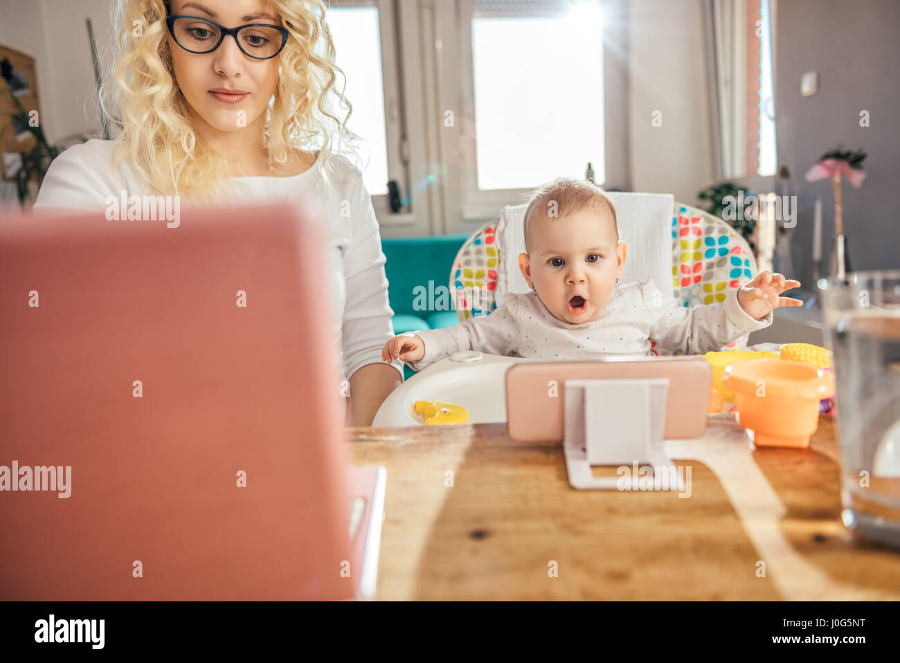 Mutter trägt Brille Büro am Laptop zu Hause arbeiten und kümmert sich um ihr baby Stockfoto