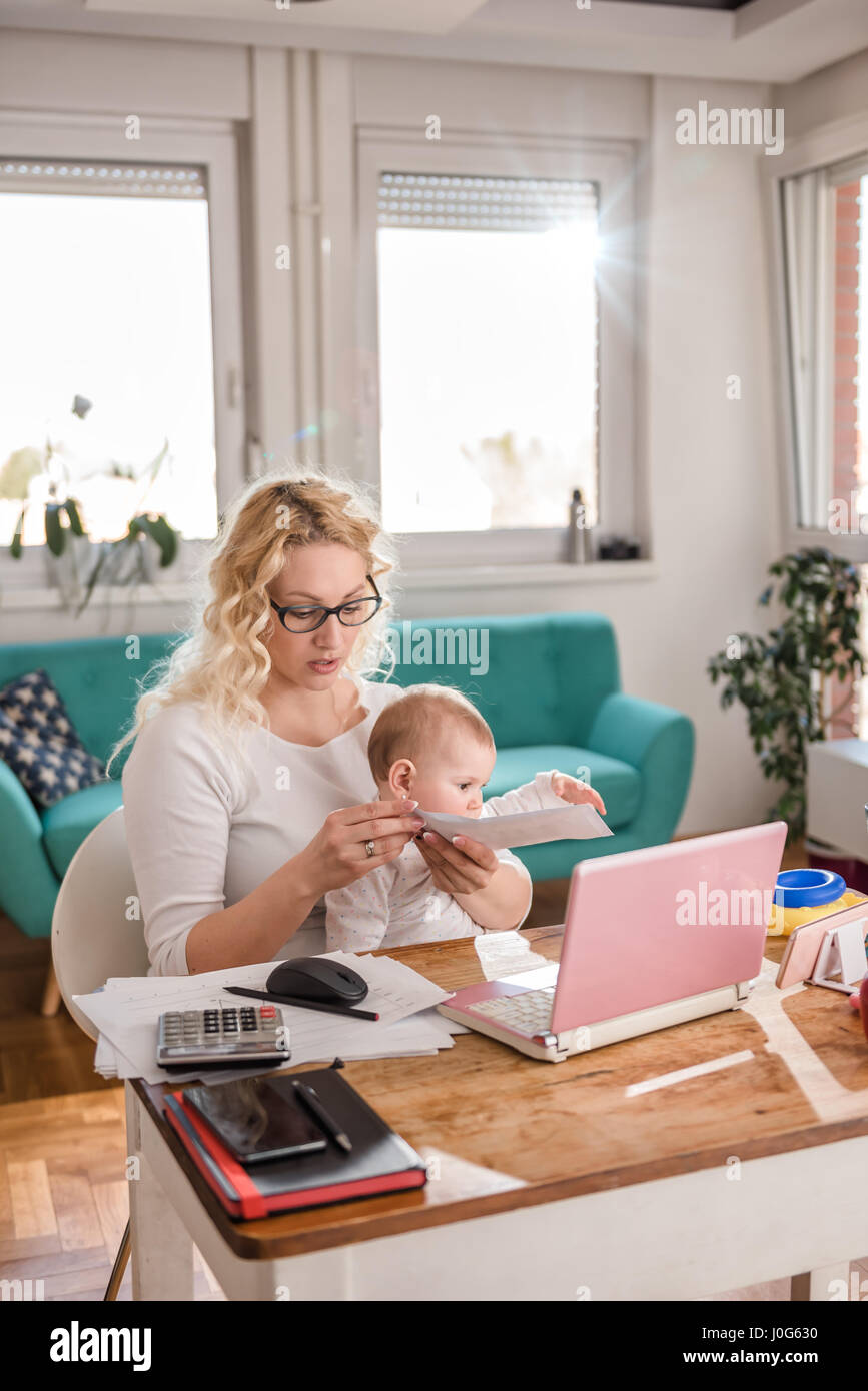 Mutter trägt Brille hält Baby und Öffnung Umschlag zu Hause im Büro Stockfoto