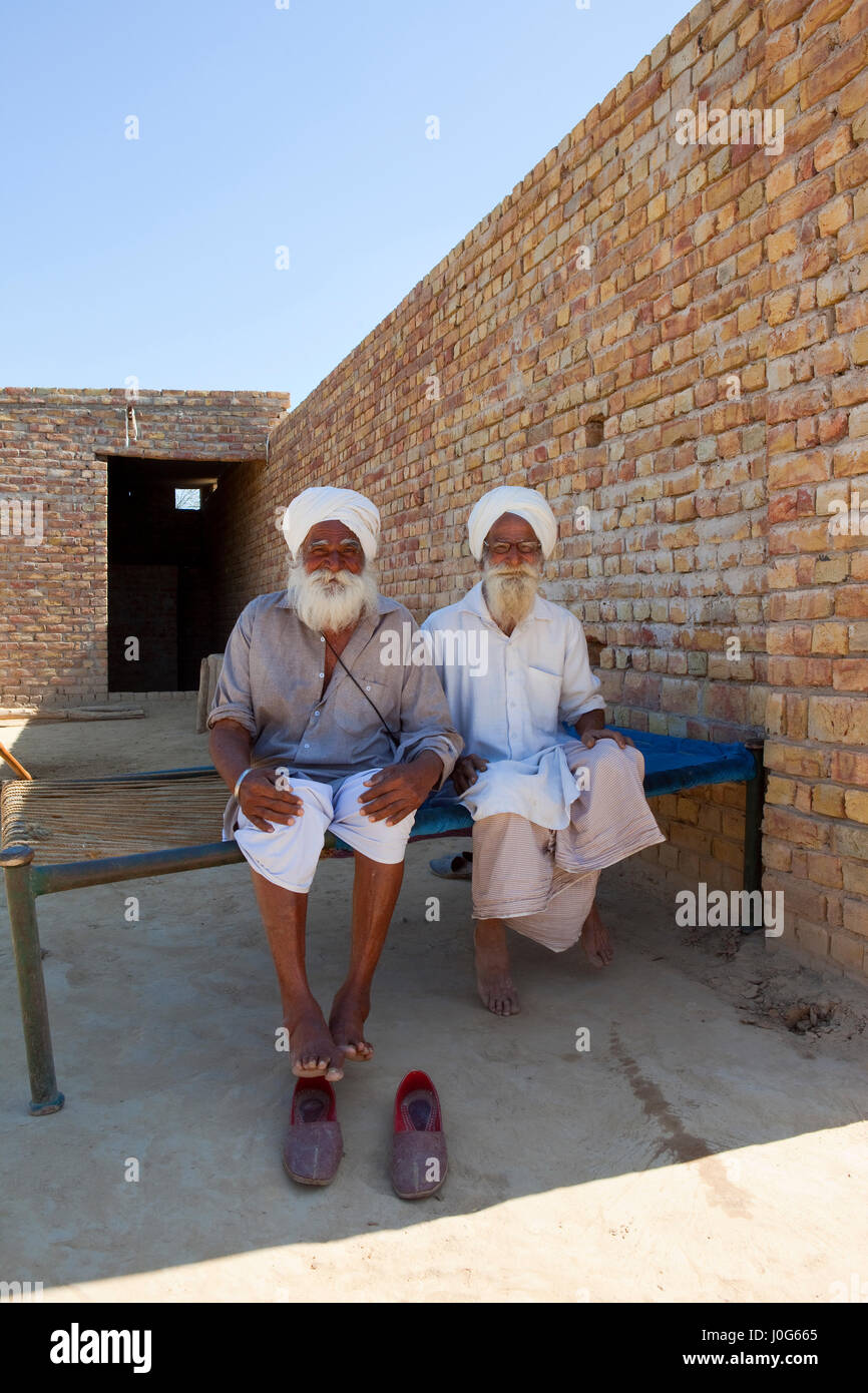 zwei traditionell gekleideten Rajasthan Bauern sitzen auf einem Bett zu Hause unter einem strahlend blauen Himmel in Indien Stockfoto