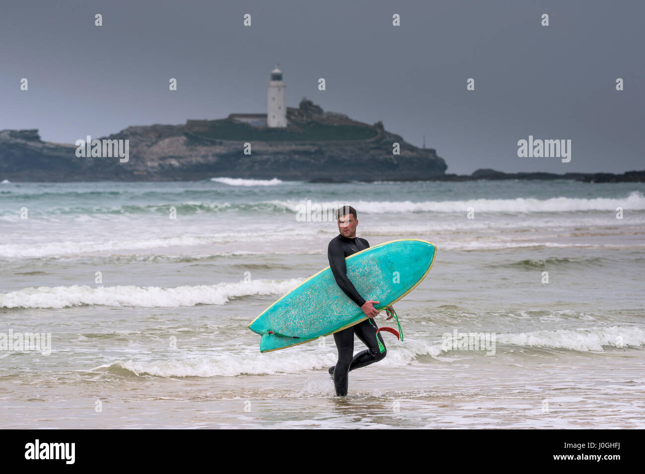 Gwithian Towans Strand Meer männliche Surfer zu Fuß aus dem Meer Godrevy Leuchtturm tragen Surfbrett Küste Küste Freizeitbeschäftigung Stockfoto