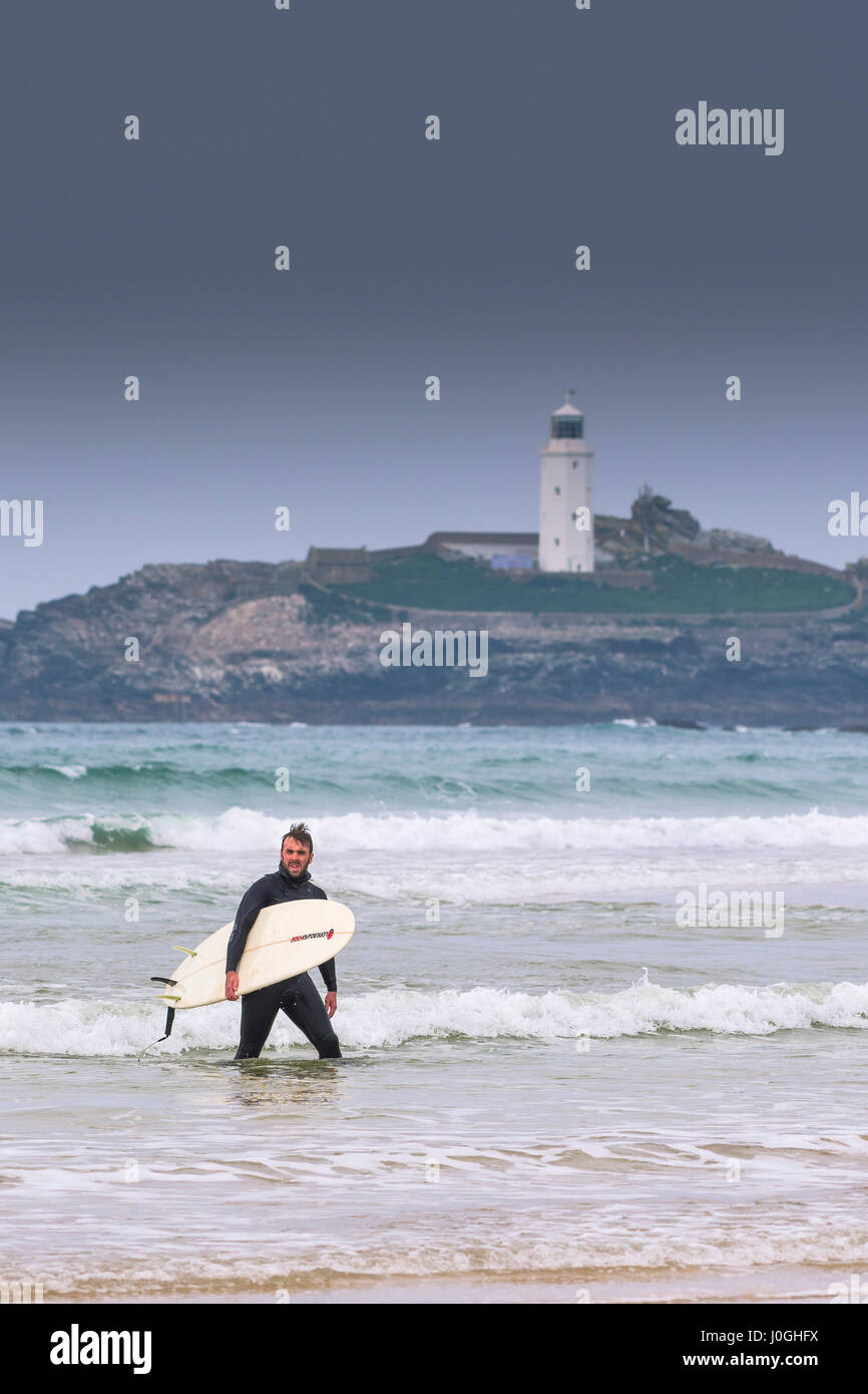 Gwithian Towans beach Surfer zu Fuß aus dem Meer Meer tragen Surfbrett Godrevy Leuchtturm Küste Küste Freizeitbeschäftigung Urlaubsaktivität Stockfoto