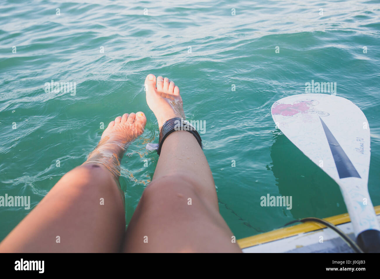 Mädchen die Beine im Wasser plantschen, beim Sitzen auf einem paddleboard Stockfoto