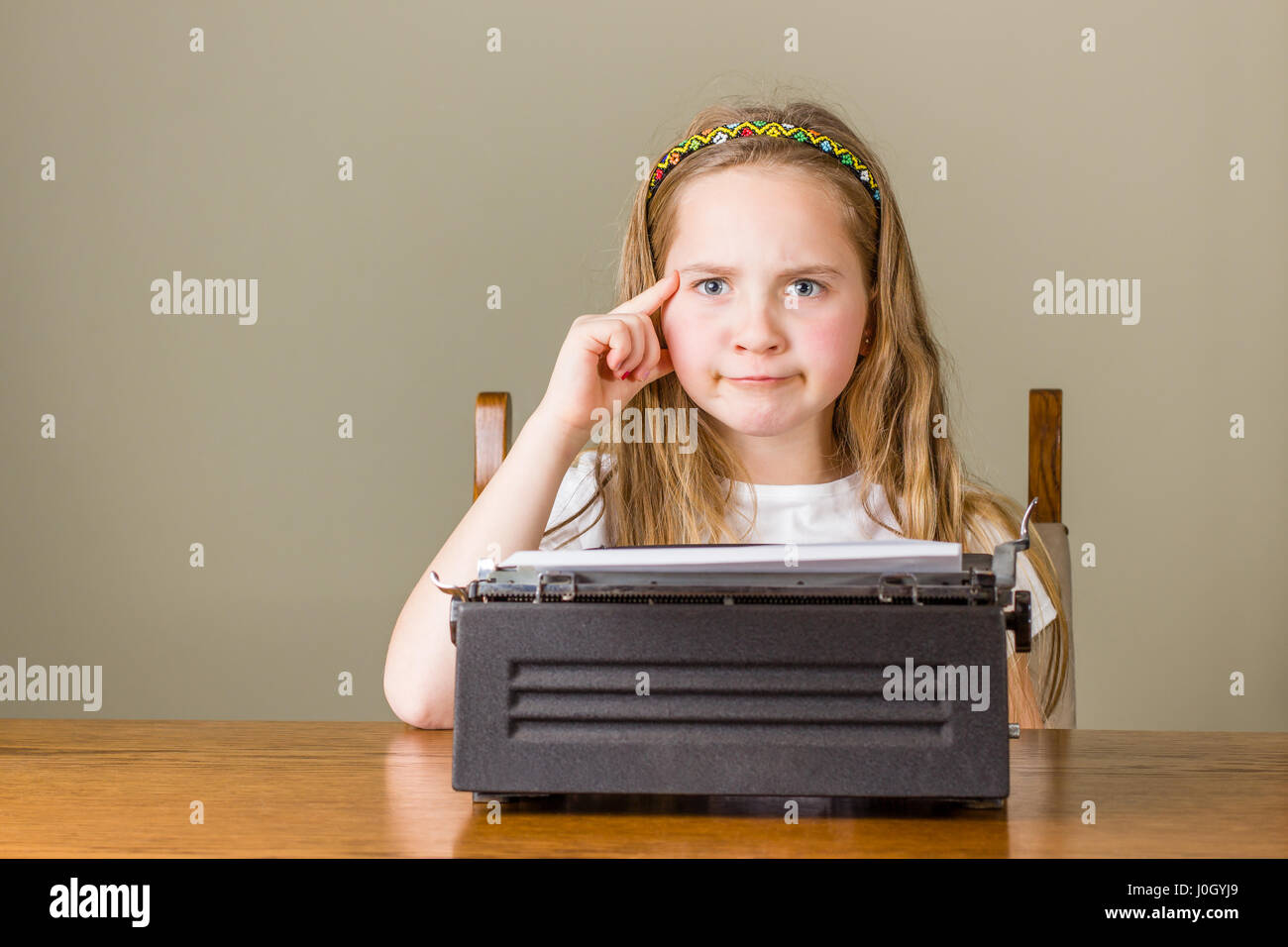 Junge blonde Mädchen schauen verwirrt hat sie auf einer schwarzen Vintage Schreibmaschine zu Hause arbeiten Stockfoto