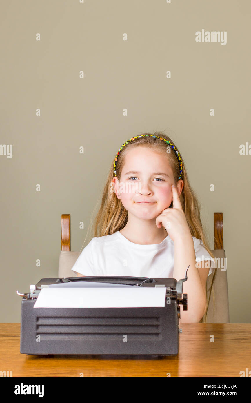 Junge blonde Mädchen denken über etwas während der Arbeit an einer schwarzen Vintage Schreibmaschine zu Hause Stockfoto
