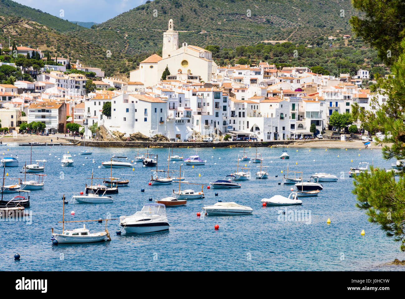 Weiß getünchten Dorf Cadaqués gekrönt von der Kirche Santa Maria mit Blick auf Boote in den blauen Gewässern des Cadaques Bucht, Cadaques, Katalonien, Spanien Stockfoto