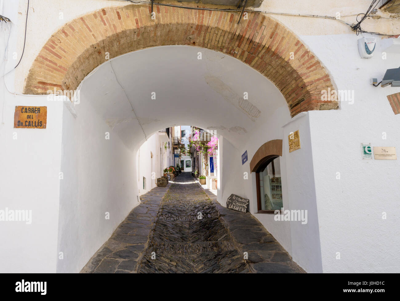 Einen Bogen Gang durch eine weiß getünchte Gebäude entlang der Carrer des nennen, bekannt für seine Fischgräten Rastell Kopfsteinpflaster Bürgersteig, Cadaques, Katalonien, Spanien Stockfoto