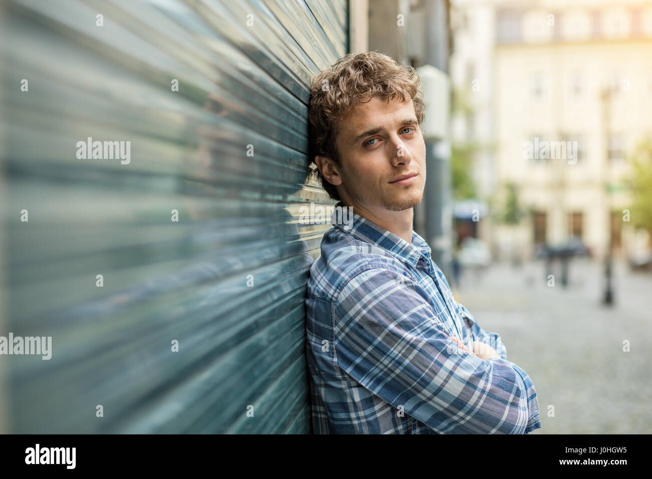 Blond und Culry Jüngling im karierten Hemd steh außerhalb neben einer Wand Stockfoto