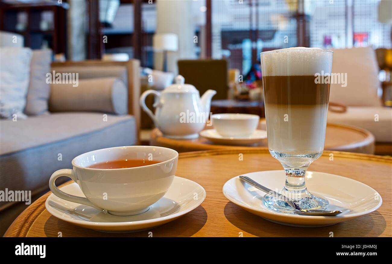 Tabelle mit Tasse schwarzer Tee und ein Glas Latte Macchiato in einer gemütlichen Umgebung Stockfoto