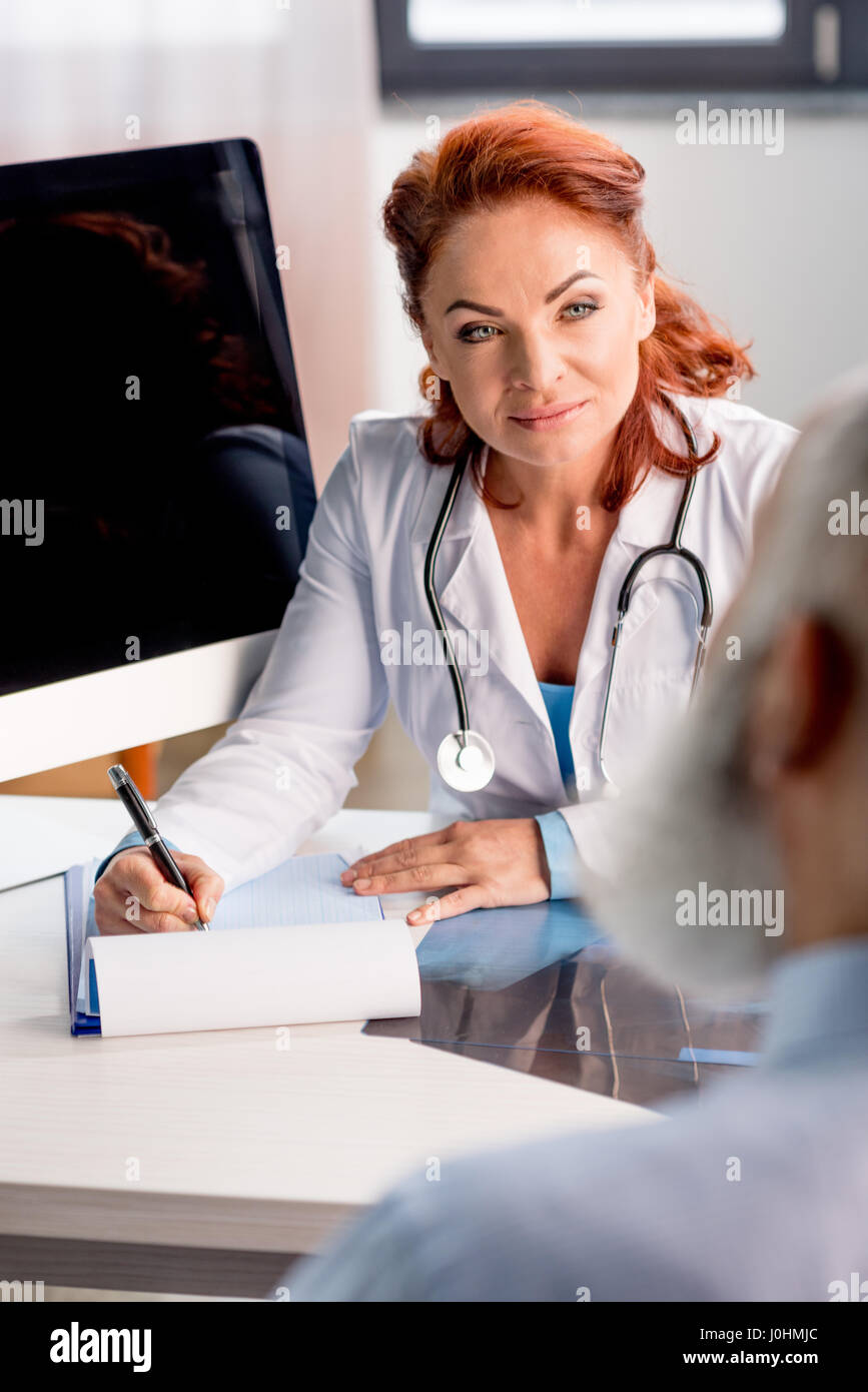 Professionelle Ärztin in Zwischenablage schreiben und mit Blick auf Patienten Stockfoto