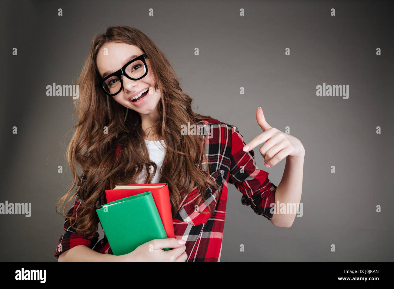 Foto der hübsche junge Frau mit Brille posiert isoliert auf grauem Hintergrund Bücher in Händen hält, und zeigt. Blick in die Kamera. Stockfoto