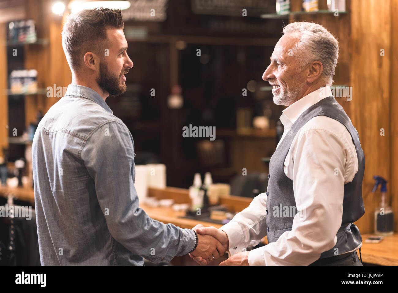 Dankbar, gealterter Mann Handshaking mit Friseur im Frisörsalon Stockfoto