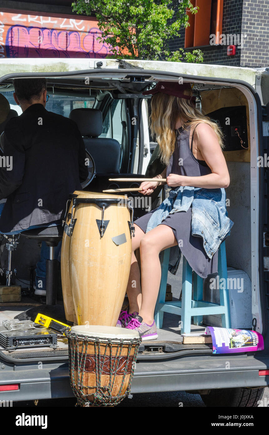 Ein Mann und eine Frau sitzen in einem Lieferwagen, die auf der Brick Lane im Osten Londons geparkt ist, Schlagzeug zu spielen. Stockfoto