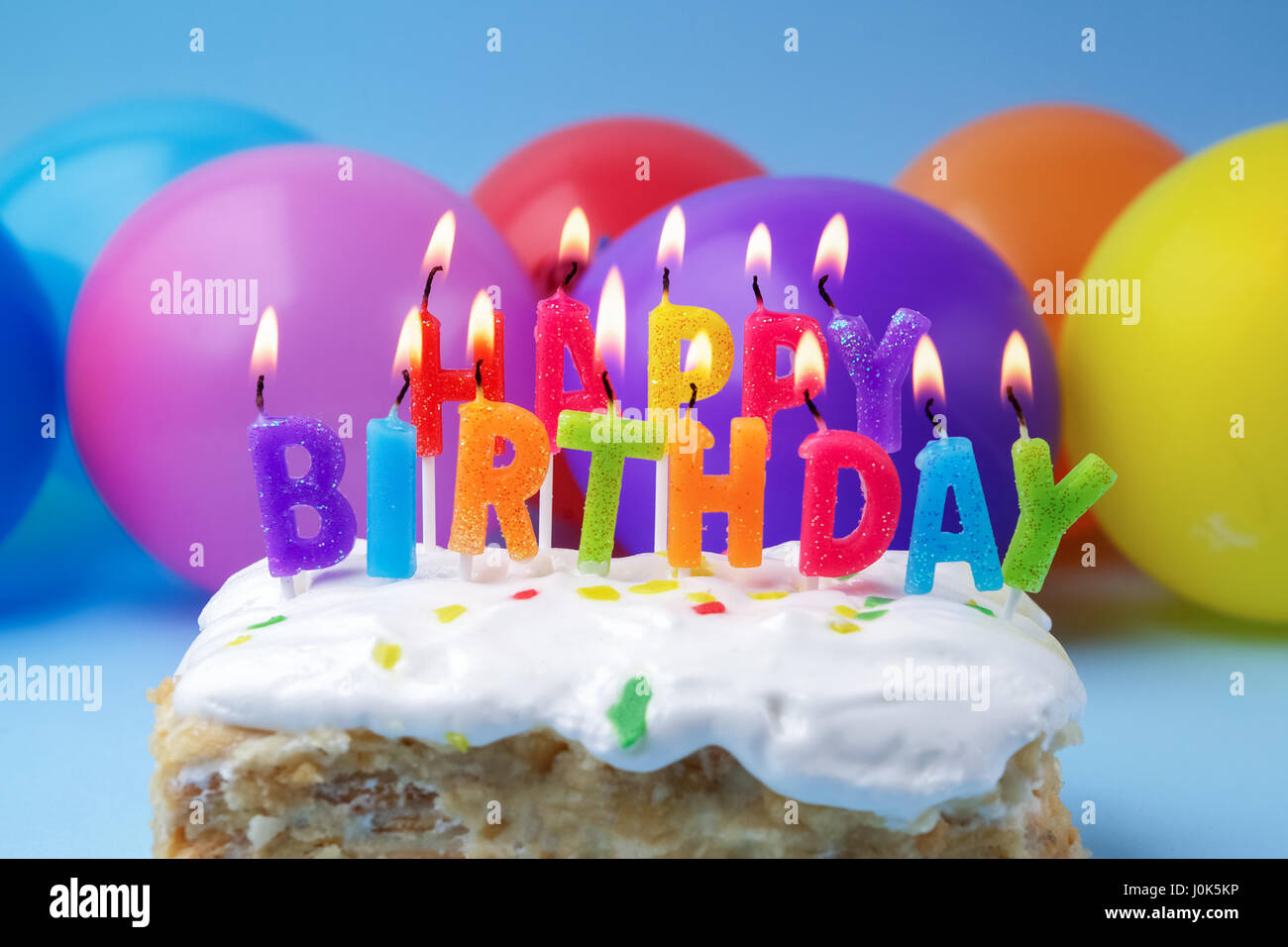 Kuchen mit Geburtstagsgrüße von brennenden Kerzen auf einem bunten  Luftballons-Hintergrund Stockfotografie - Alamy