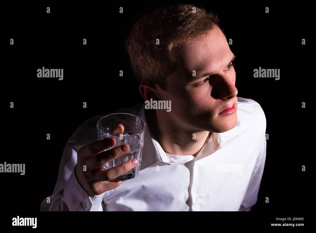 Junger Mann in einem Hemd mit blonden oder hell braune Haare halten einen Whisky oder verzierten Wasserglas Stockfoto