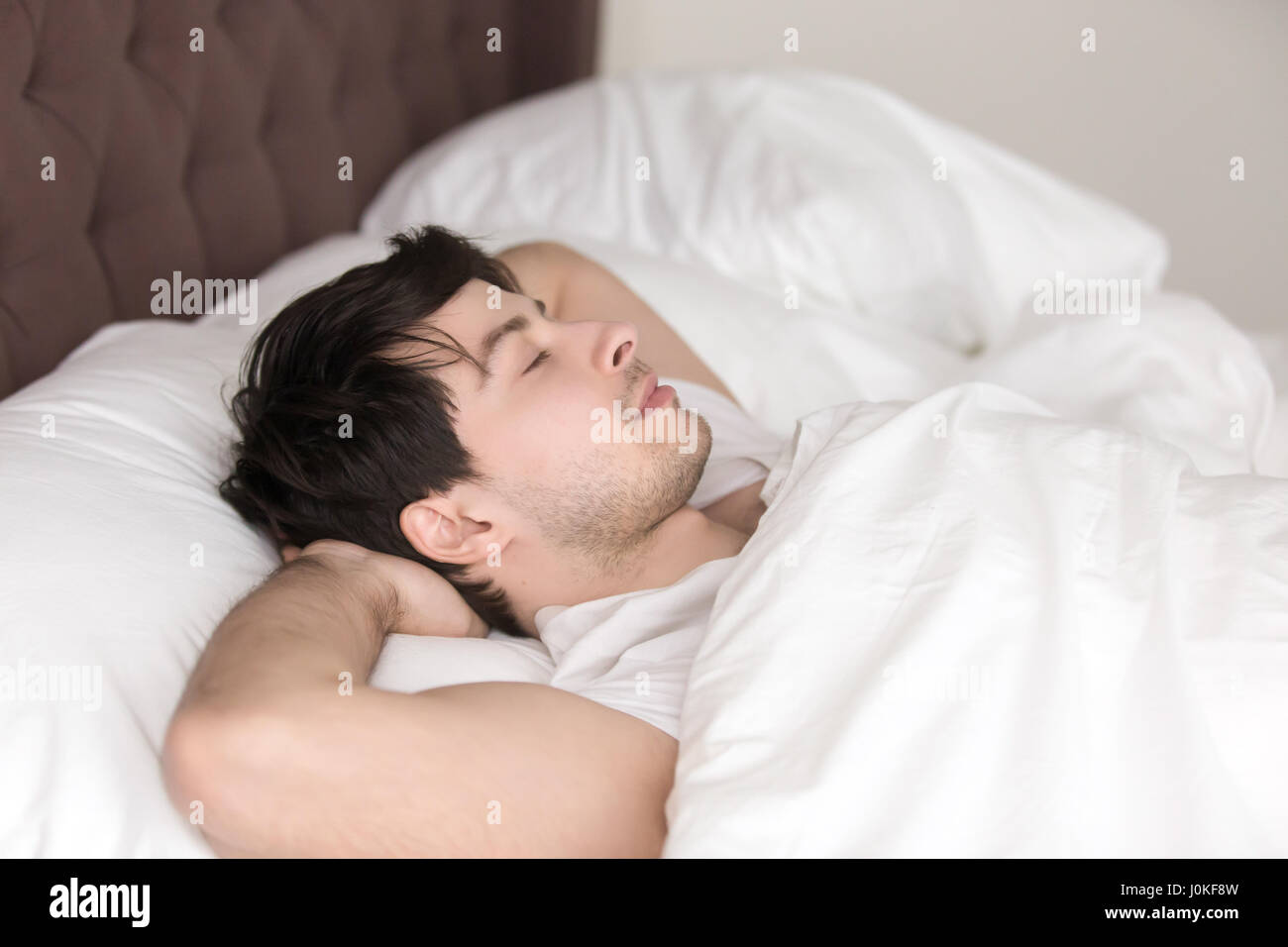 Schönen jungen Mann ruht allein im Bett mit geschlossenen Augen Stockfoto