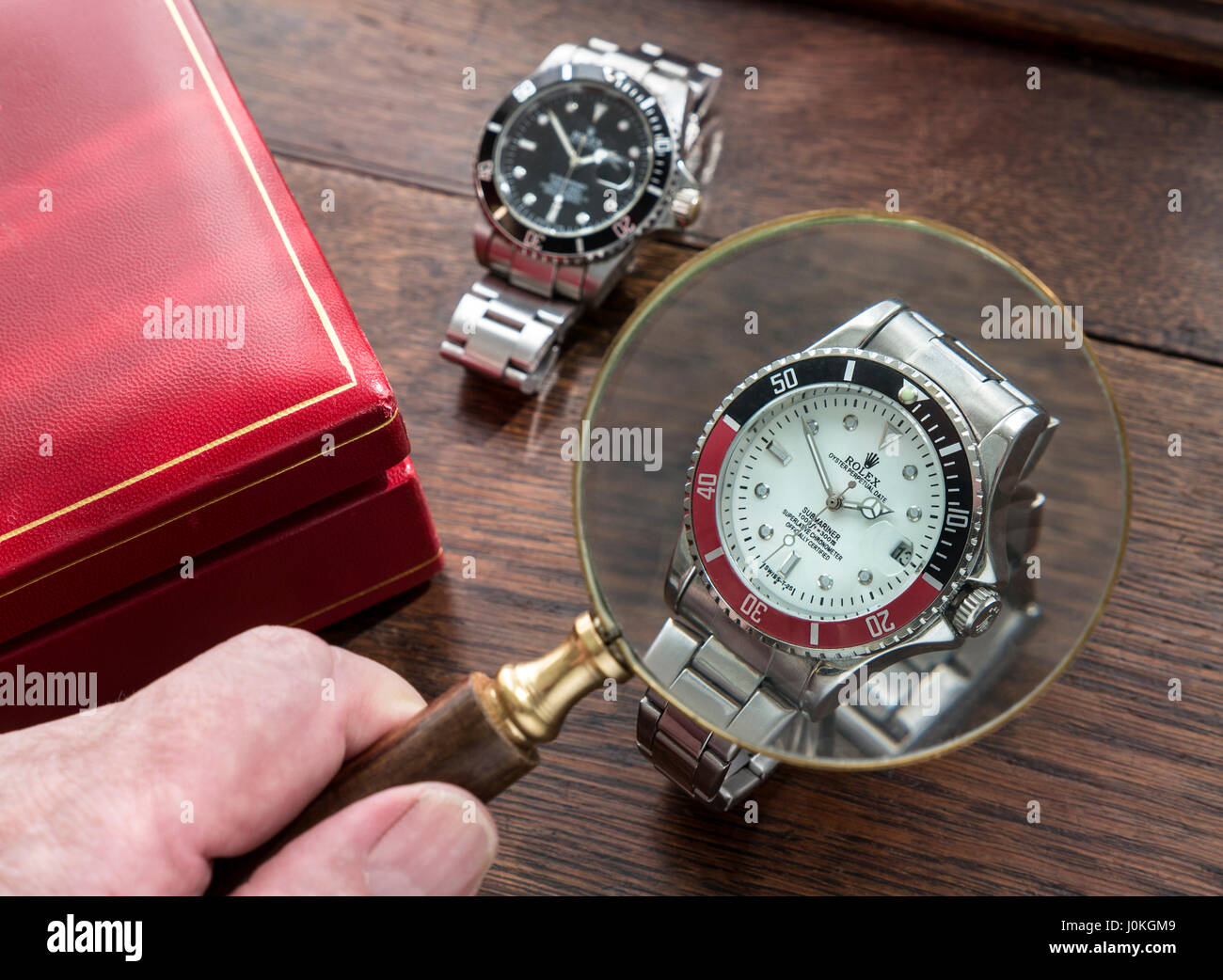 ROLEX GEFÄLSCHTE UHREN Vergrößerungsglas und gefälschte Replik Kopie gefälschte Männer Rolex Uhren auf alten hölzernen Schreibtisch mit rotem Leder Uhrengehäuse Stockfoto