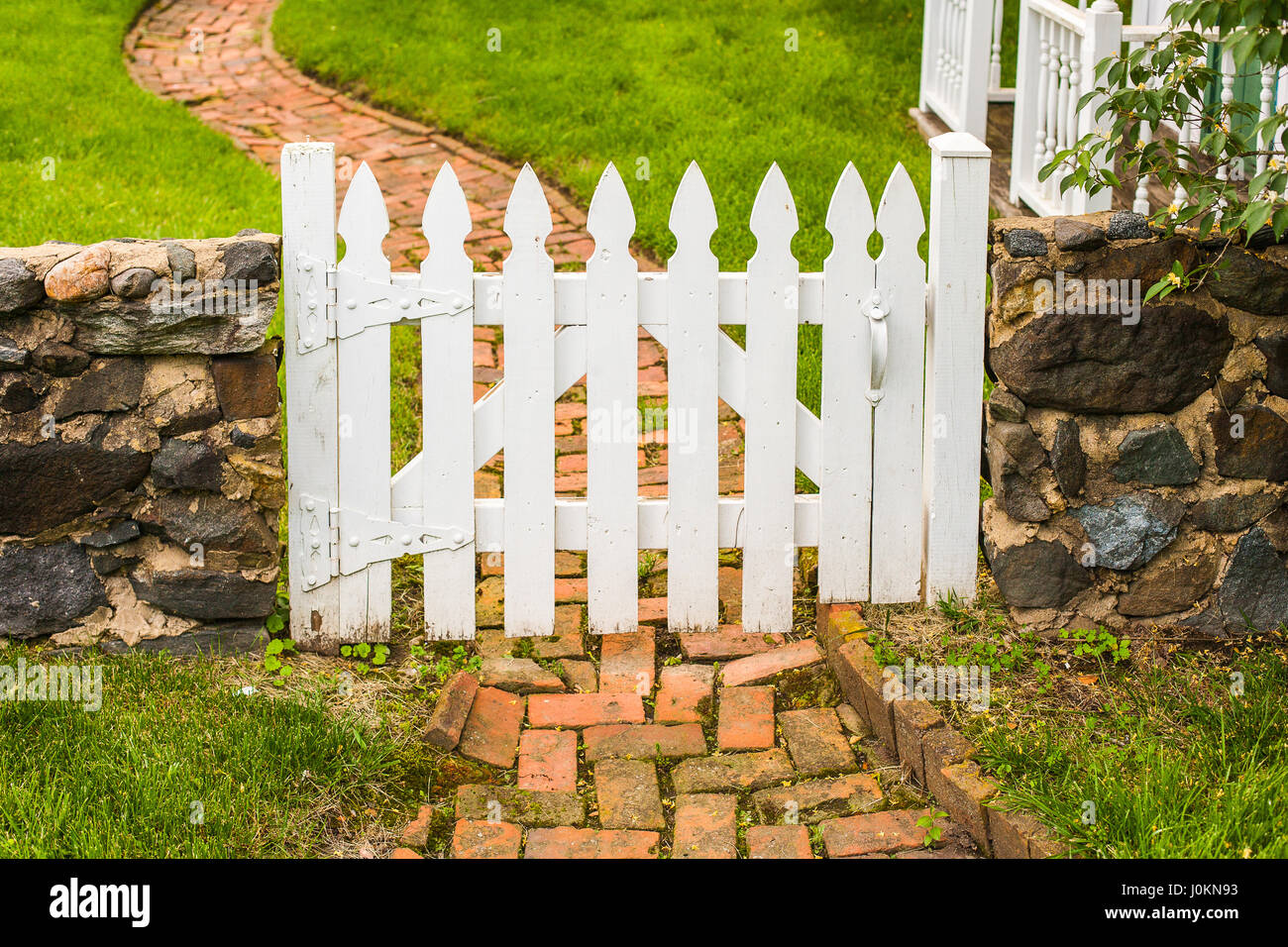 Einem weißen hölzernen Latten Tor in einer niedrigen Steinmauer über einen gewundenen Ziegel Gartenweg. Stockfoto