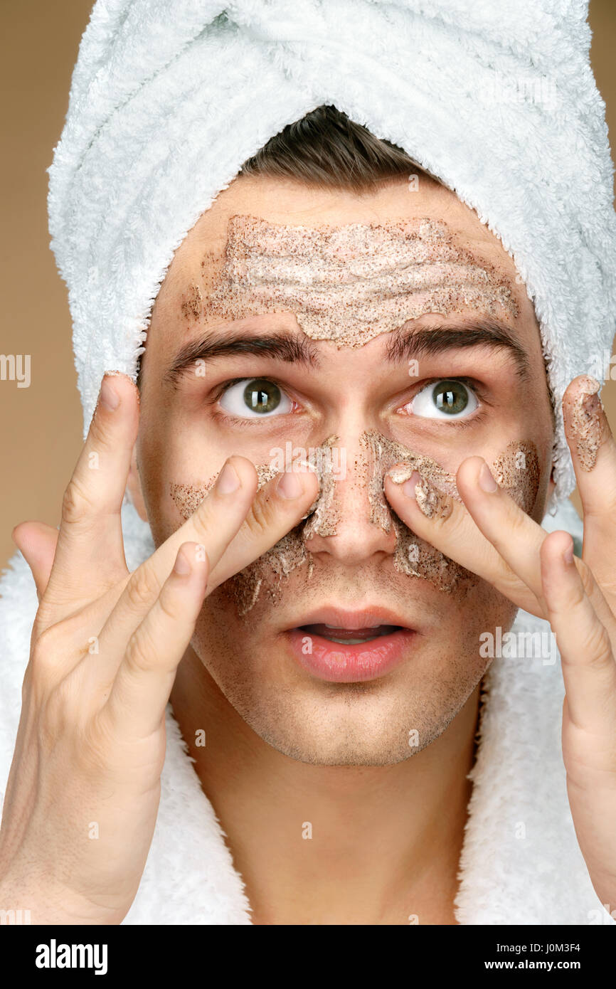Gut aussehender Mann reinigt Gesicht Peeling auf der Haut. Nahaufnahme des jungen Mannes mit Handtuch auf dem Kopf. Pflege selbst Stockfoto