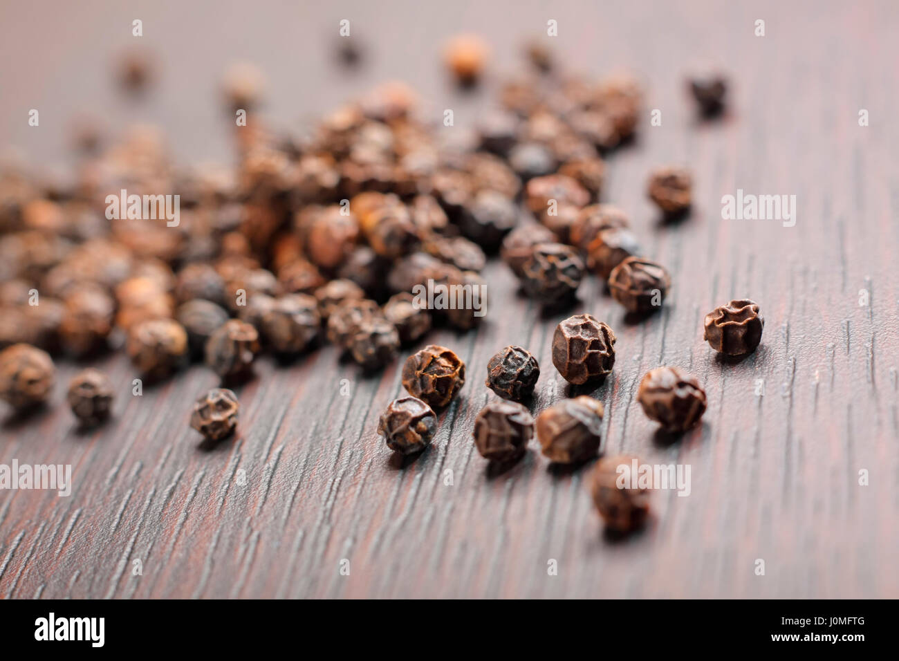 Schwarze Pfefferkörner (Piper Nigrum) auf dunklen Tisch. Nahaufnahme Foto. Stockfoto