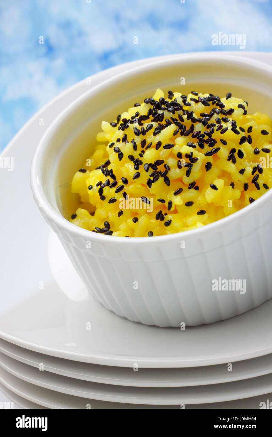 Töpfchen von weißen Langkornreis (gekocht mit Curcuma) gefüllt und schwarze Sesam Topping über Stapel von Platten Stockfoto