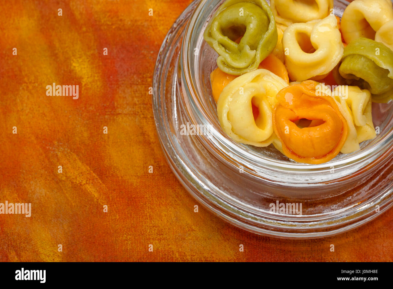 Frisch gekochte Tortellini (mit Fleisch, Tomaten und Spinatfüllung) in Glasschüssel über bemalte Textilien Hintergrund. Stockfoto