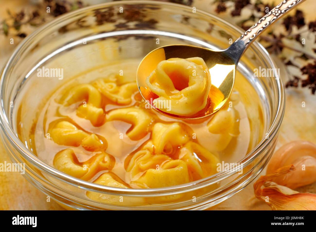 Frisch gekochte Tortellini in Glasschale mit Brühe. Einzelne Tortellini auf Löffel. Stockfoto