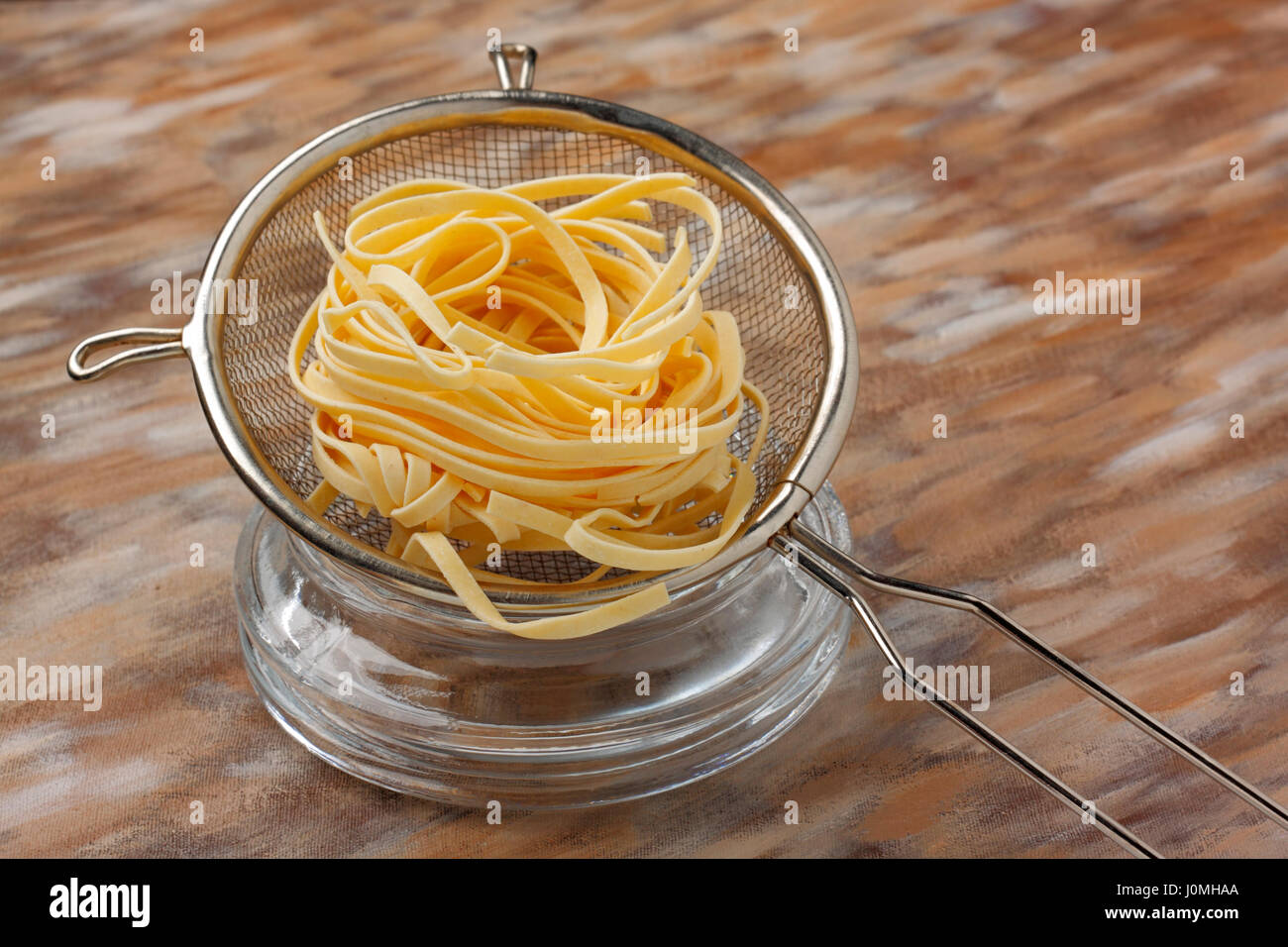 Rohe Nudeln Nudeln in Metall Küche Sieb über bemalte Textilien Hintergrund Stockfoto