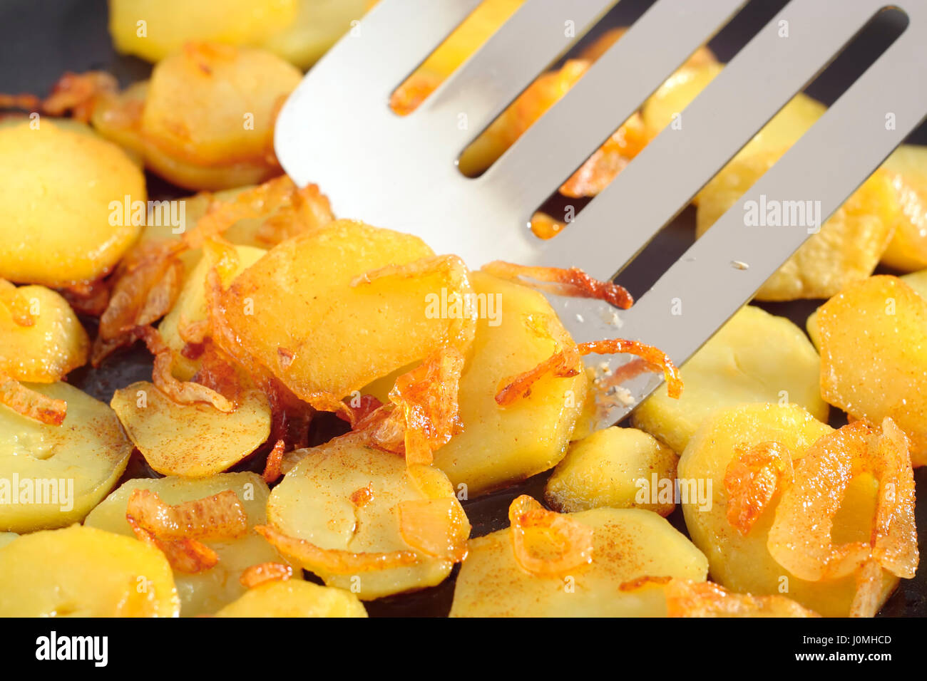 Die Nahaufnahme auf gebratenen Kartoffeln Scheiben mit Zusatz von fein gehackte Zwiebel. Im Zentrum des Rahmens der Spachtel Metall Küche. Stockfoto