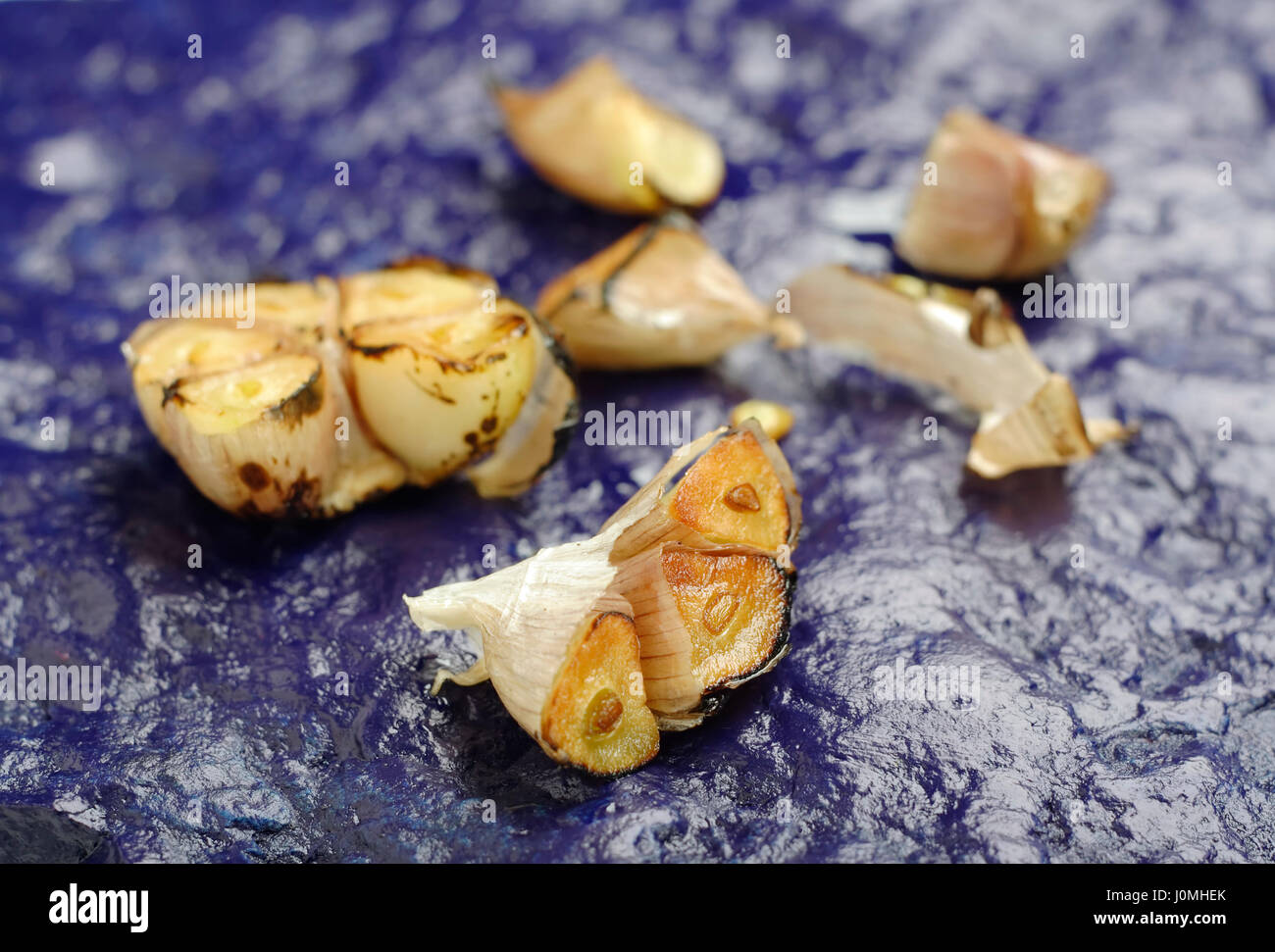 Nahaufnahme auf gebratenen Knoblauchzehe auf blau bemalten Stein liegen. Schärfe auf ersten geschnittenen Knoblauch. Stockfoto