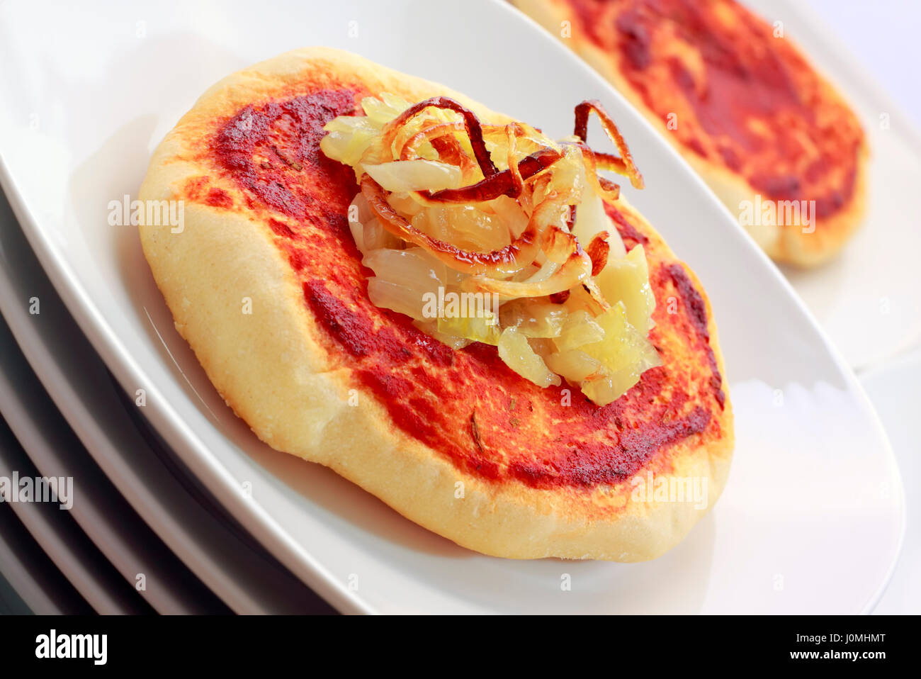 Kleine Pizza (Pizzette) mit gebratenen Zwiebeln und Tomaten Sauce auf einem Stapel von weißen Platten. Schräg zu schießen. Stockfoto