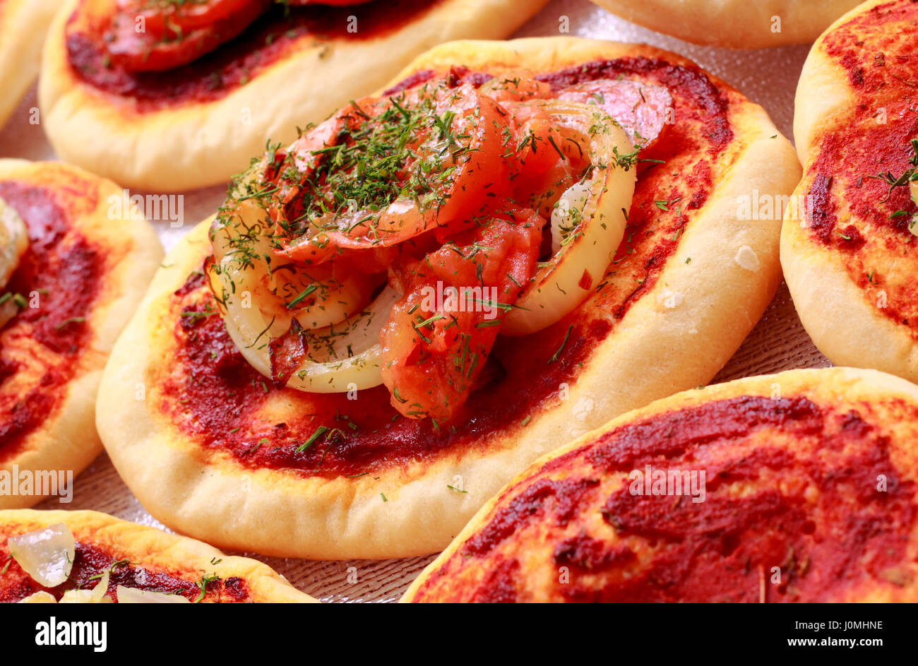 Kleine Pizzas (Pizzette) mit Kräutern, in Scheiben geschnittene Wurst, Zwiebeln und Tomaten. Schräg zu schießen. Stockfoto